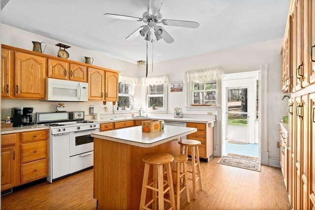 kitchen featuring light wood finished floors, white appliances, light countertops, and a kitchen bar