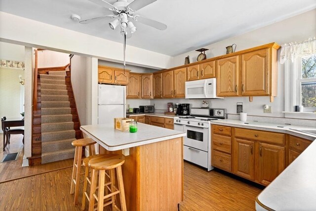 kitchen featuring white appliances, visible vents, a kitchen island, light countertops, and light wood-type flooring