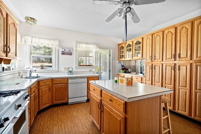 kitchen featuring glass insert cabinets, wood finished floors, a sink, white appliances, and light countertops