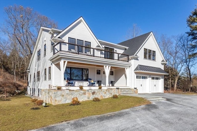 modern farmhouse style home with a front yard, a balcony, an attached garage, covered porch, and aphalt driveway