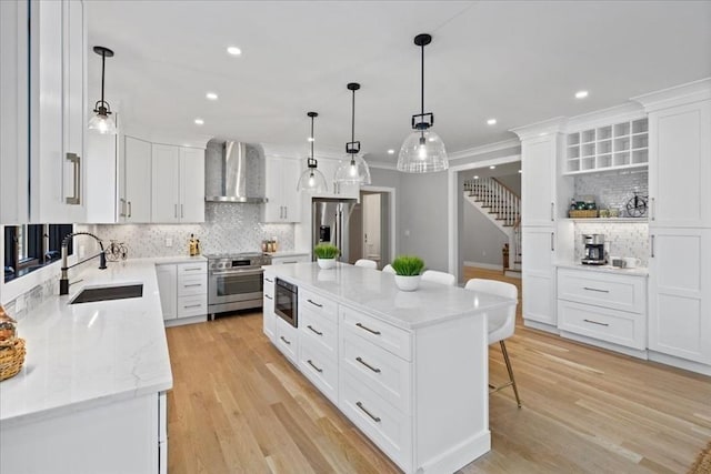 kitchen featuring a kitchen bar, a sink, light wood-style floors, appliances with stainless steel finishes, and wall chimney range hood