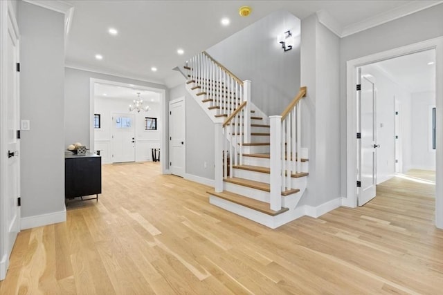 foyer entrance featuring light wood finished floors, crown molding, stairs, recessed lighting, and a notable chandelier