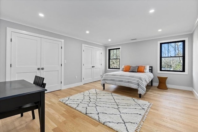 bedroom with light wood-type flooring, two closets, crown molding, and baseboards