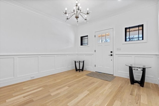 entrance foyer with a wainscoted wall, an inviting chandelier, crown molding, a decorative wall, and light wood-type flooring