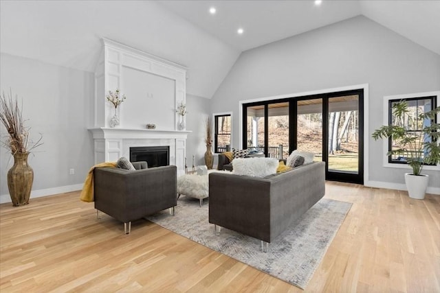 living area with a glass covered fireplace, high vaulted ceiling, light wood-type flooring, and baseboards