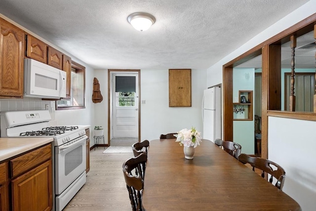 kitchen with white appliances, brown cabinets, light wood-style flooring, a textured ceiling, and light countertops