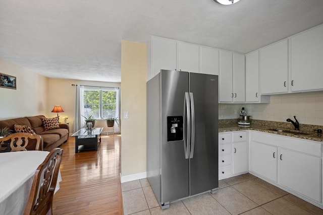 kitchen with stainless steel fridge with ice dispenser, open floor plan, a sink, dark stone counters, and tasteful backsplash