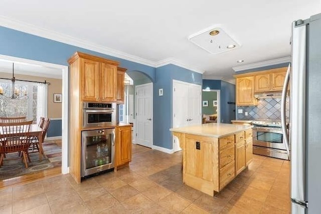 kitchen with crown molding, appliances with stainless steel finishes, backsplash, a center island, and beverage cooler