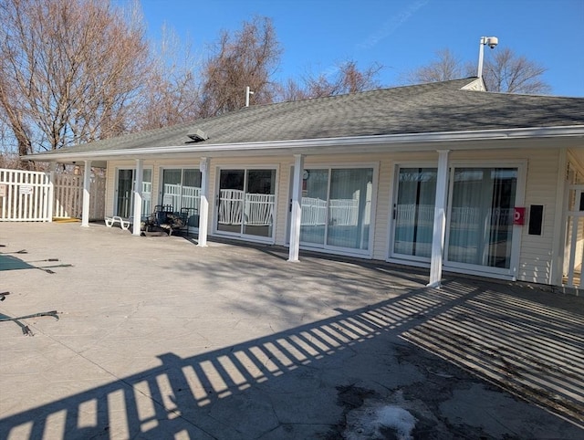 rear view of property featuring a patio area, fence, and a shingled roof