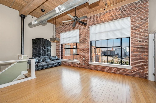 unfurnished living room with beam ceiling, hardwood / wood-style flooring, brick wall, wood ceiling, and a towering ceiling