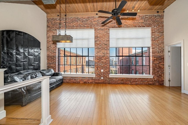 unfurnished living room with hardwood / wood-style floors, wooden ceiling, plenty of natural light, and brick wall