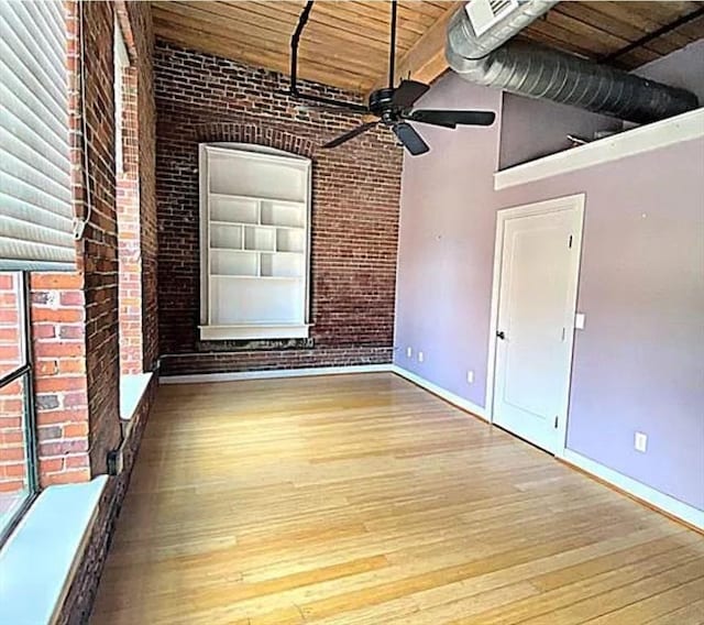 spare room with a ceiling fan, hardwood / wood-style flooring, brick wall, wooden ceiling, and baseboards