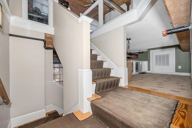 stairway with wood finished floors, baseboards, and a towering ceiling