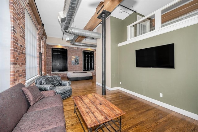 living area with brick wall, baseboards, and wood finished floors