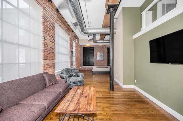 living room featuring visible vents, wood finished floors, brick wall, baseboards, and a towering ceiling