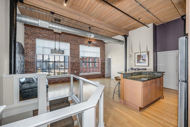 kitchen featuring a high ceiling, brick wall, light wood-type flooring, and freestanding refrigerator