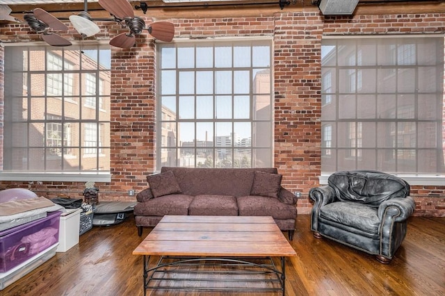 living room with ceiling fan, wood finished floors, and brick wall