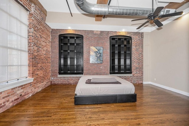 bedroom featuring baseboards, wood finished floors, and brick wall