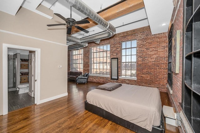 bedroom featuring wood finished floors, baseboards, brick wall, a towering ceiling, and connected bathroom