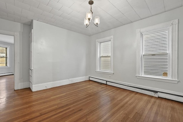 unfurnished room with a notable chandelier, a baseboard radiator, baseboards, and wood finished floors