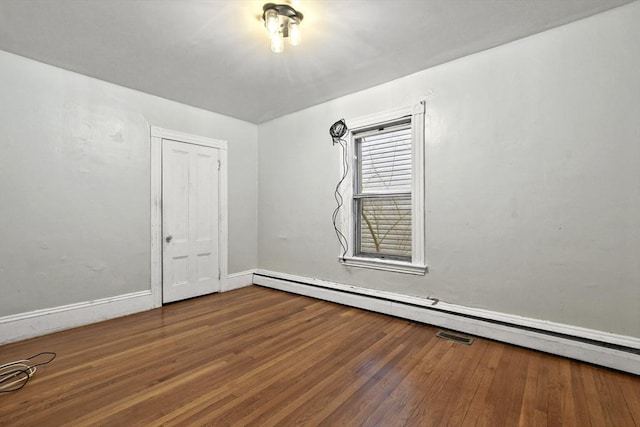 empty room featuring a baseboard heating unit, baseboards, and wood finished floors