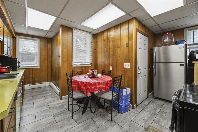 kitchen with black appliances, a baseboard heating unit, wood walls, light countertops, and a paneled ceiling