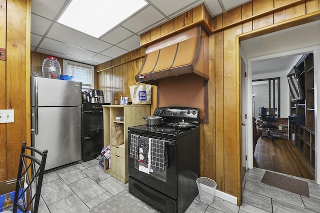 kitchen featuring premium range hood, a drop ceiling, wood walls, freestanding refrigerator, and black electric range