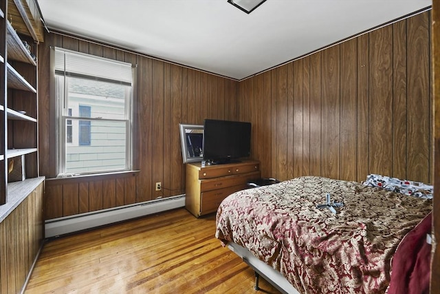 bedroom with baseboard heating, wood walls, and light wood-style floors