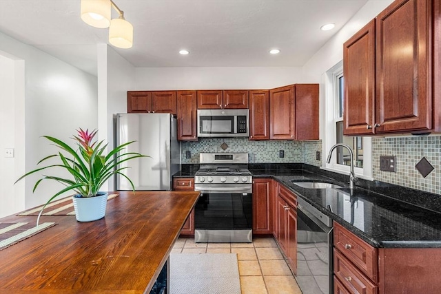 kitchen featuring sink, dark stone countertops, pendant lighting, light tile patterned floors, and appliances with stainless steel finishes