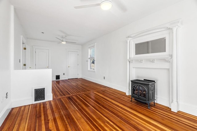 unfurnished living room featuring hardwood / wood-style floors, a wood stove, and ceiling fan