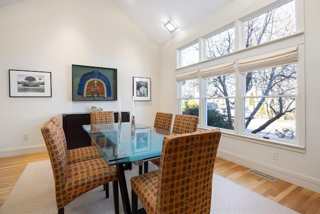 dining area with high vaulted ceiling and light hardwood / wood-style floors