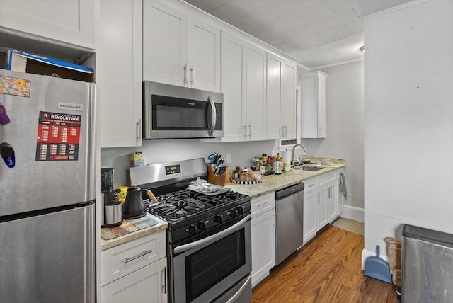 kitchen with stainless steel appliances, light wood-style flooring, ornamental molding, white cabinetry, and a sink