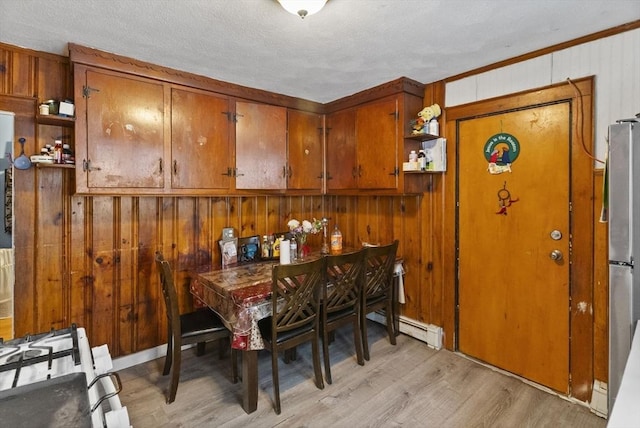 dining space featuring a textured ceiling, baseboard heating, wood walls, and light wood-type flooring