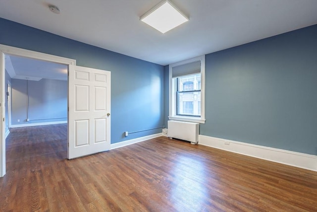 empty room featuring baseboards, wood finished floors, and radiator