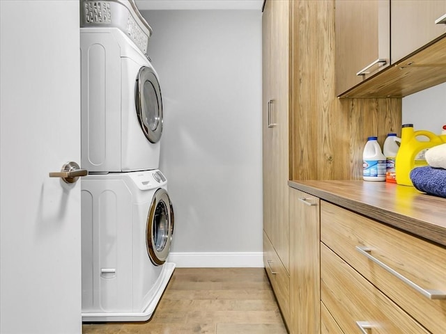 washroom with baseboards, cabinet space, light wood-style flooring, and stacked washer / dryer