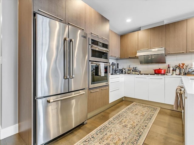 kitchen with modern cabinets, light wood-style flooring, stainless steel appliances, light countertops, and decorative backsplash