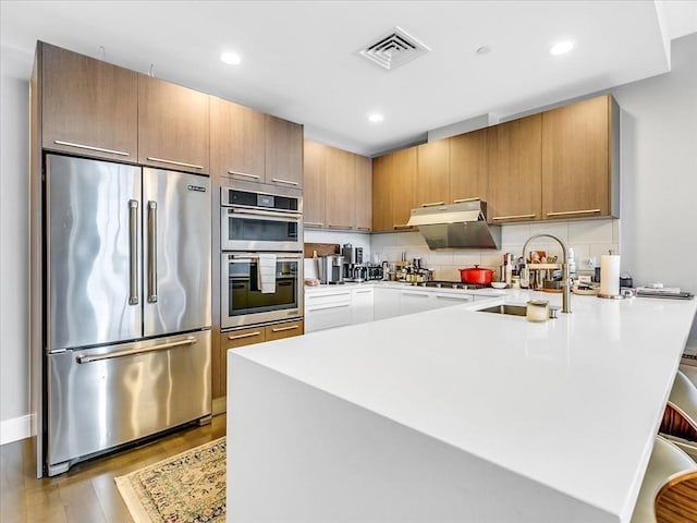 kitchen featuring wood finished floors, visible vents, a peninsula, a sink, and appliances with stainless steel finishes