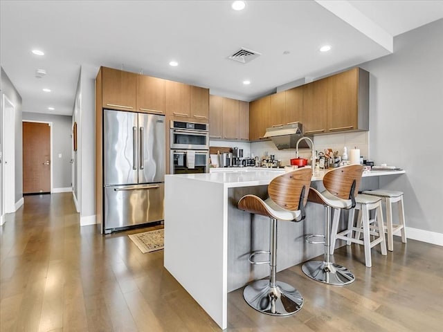 kitchen featuring visible vents, a peninsula, stainless steel appliances, light countertops, and under cabinet range hood