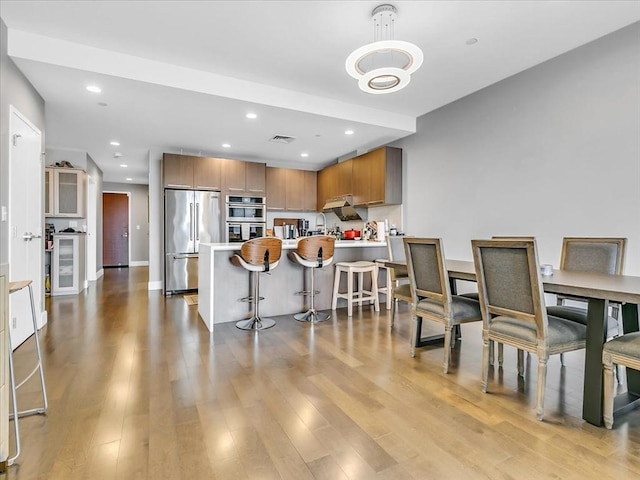 kitchen featuring wood finished floors, a peninsula, stainless steel appliances, a kitchen breakfast bar, and brown cabinets