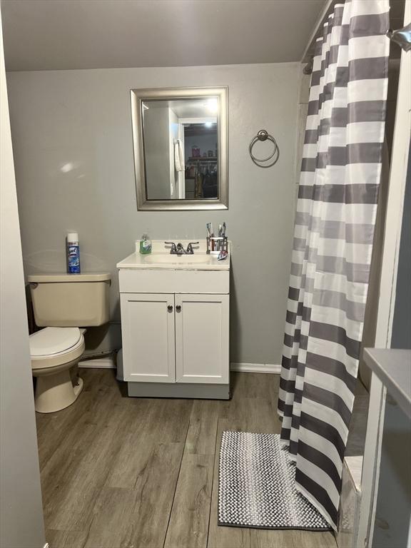 full bathroom featuring curtained shower, toilet, vanity, wood finished floors, and baseboards