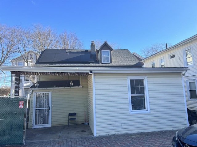 back of house featuring a chimney and solar panels