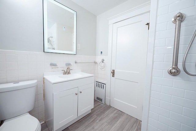 bathroom featuring tile walls, hardwood / wood-style floors, radiator heating unit, vanity, and toilet