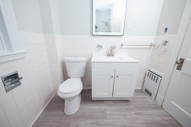 bathroom featuring radiator heating unit, wood-type flooring, tile walls, vanity, and toilet