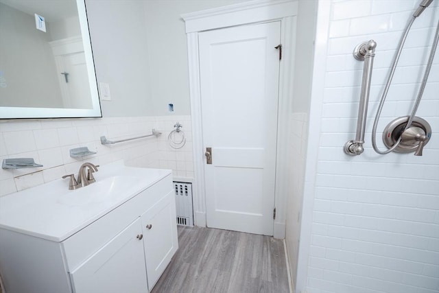 bathroom featuring radiator heating unit, hardwood / wood-style floors, tiled shower, and tile walls