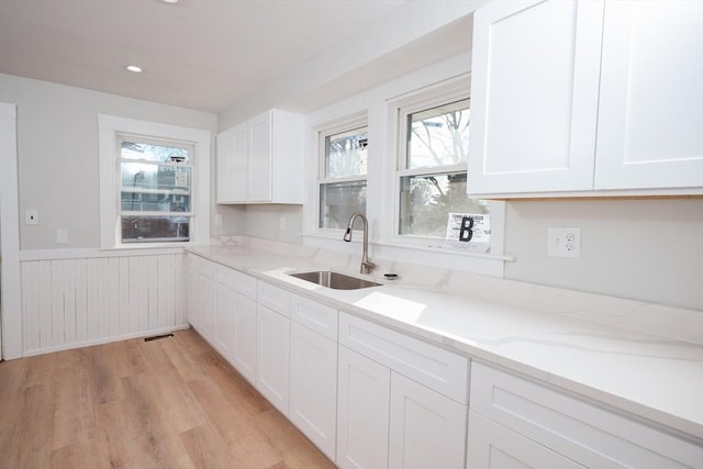 kitchen with light stone countertops, sink, white cabinets, and light hardwood / wood-style floors