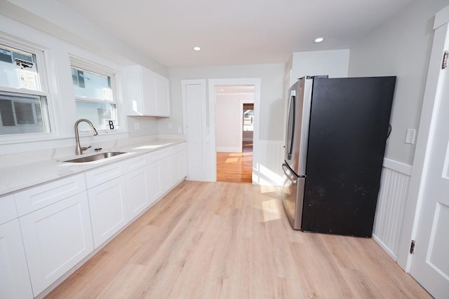 kitchen with sink, light hardwood / wood-style flooring, stainless steel refrigerator, light stone countertops, and white cabinets