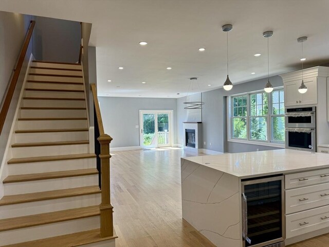 kitchen with beverage cooler, stainless steel double oven, recessed lighting, white cabinetry, and a glass covered fireplace