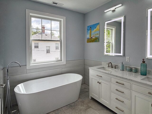 full bath with double vanity, a freestanding bath, wainscoting, and tile walls