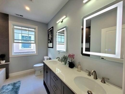 full bathroom featuring plenty of natural light, toilet, double vanity, and baseboards
