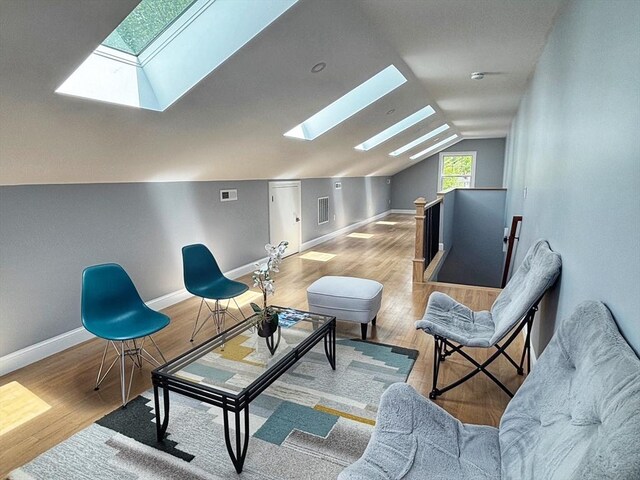 sitting room with a skylight, an upstairs landing, vaulted ceiling, baseboards, and wood finished floors